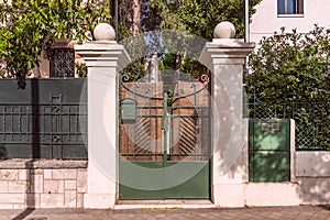 Portal of an urban single-family house with a metal fence with dark green painted wrought iron works