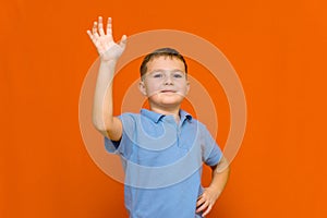 Portarait of caucasian happy smiling little boy with raised hand on orange wall