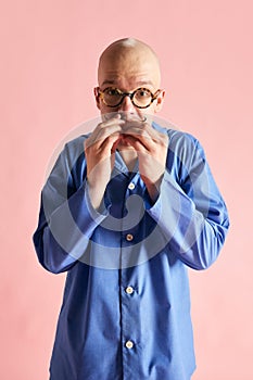 Portarit of funny man in pajama holding hand near mouth and looking at camera over pastel rose background. photo