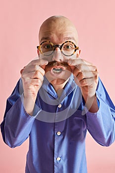 Portarit of funny man in pajama looking at camera and straightensand curls mustaches over pastel rose background. photo