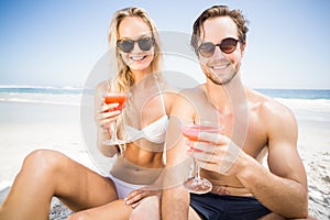 Portarit of young couple in sunglasses having cocktail on the beach