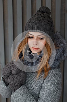 Porter of a charming cute young woman in a knitted hat in a gray winter coat with fur in vintage mittens