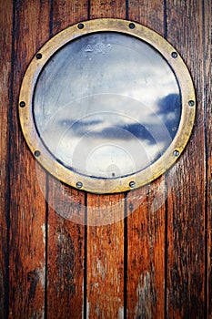 Porthole ship window on wooden doors, sky reflection
