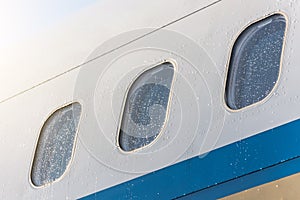 Porthole windows of an airplane wet weather in rain drops of water, close-up.