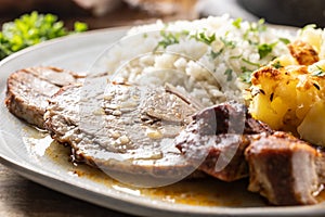 A portion of baked juicy neck on a plate with a side dish of potatoes and rice and a sauce with baked goods