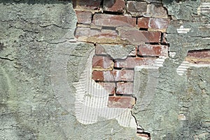 A portion of a broken plaster wall with with underlying exposed red bricks