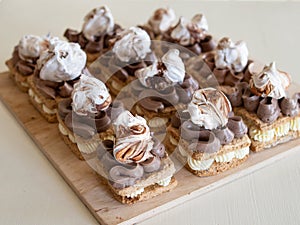 Portion cakes of meringue and cocoa butter cream in square form on a wooden stand, a piece of cake on a light wooden