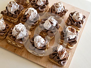 Portion cakes of meringue and cocoa butter cream in square form on a wooden stand, a piece of cake on a light wooden background.