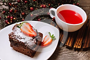 A portion of chocolate brownie and a cup of fruit tea to take time a have a break. On a wooden table top, a hot cup of tea. Wild a