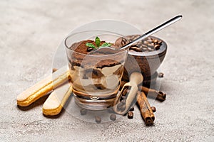 Portion of Classic tiramisu dessert in a glass cup, scoop full of coffee and cinnamon sticks on concrete background
