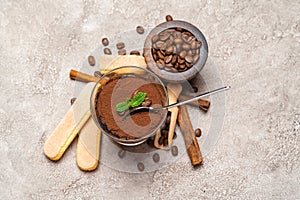 Portion of Classic tiramisu dessert in a glass cup, scoop full of coffee and cinnamon sticks on concrete background