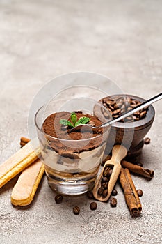 Portion of Classic tiramisu dessert in a glass cup, scoop full of coffee and cinnamon sticks on concrete background