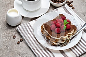 Portion of Classic tiramisu dessert with raspberries and cup of coffee and cream or milk on grey concrete background