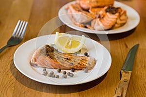 Portion of cooked salmon fillet with lemon slice on white plate