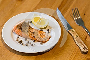 Portion of cooked salmon fillet with lemon slice on white plate