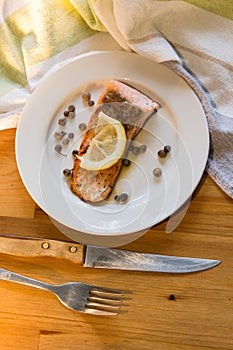 Portion of cooked salmon fillet with lemon slice on white plate