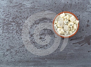 Portion of crumbled blue cheese on a in a small bowl offset on a gray background