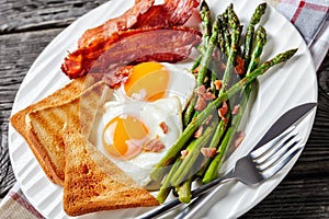 A portion of fried eggs, bacon, toasts, asparagus