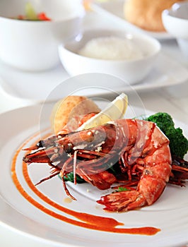 Portion of grilled big prawn on the white plate ready to serve at restaurant with sauce and broccoli