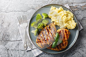 portion of grilled chicken breast with a side dish of mashed potatoes and broccoli close-up in a plate. Horizontal top view