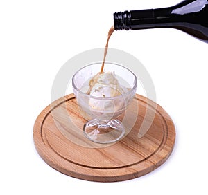 A portion of ice cream in a crystal glass on a wooden board is poured with liquor from a bottle