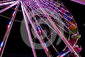 Portion of a lighted Ferris wheel at night with multicolored gondolas