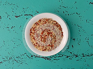 A portion of long grain brown rice and red rice in a white bowl atop a green and black tabletop