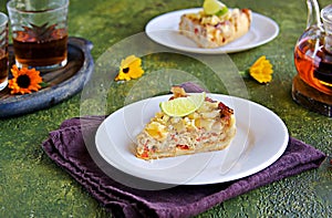 Portion of open unsweetened shortcrust pastry pie with tuna, sweet red pepper and cheese on a white plate on a green concrete