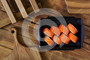 A portion of Philadelphia sushi roll in a black open cardboard box on an eco-friendly vintage pine board table next to a wooden