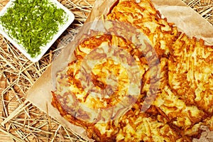 Portion of potato hash brown served with dry hay and sour-cream with dill on wooden board. Country style. Close up. Indoor shot