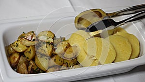 Portion potatoes of two types on one plate. Rectangular white plate with iron tongs for serving rustic potatoes with