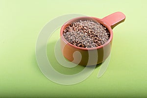 A portion of raw buckwheat in a clay bowl on a green background