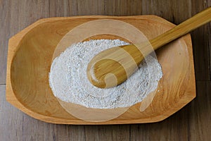 Portion of raw whole wheat flour, wooden bowl, wooden table top view