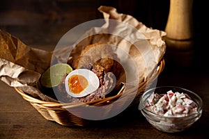 Portion of Scotch egg and pico de gallo sauce served on Ñraft paper and wicker basket.