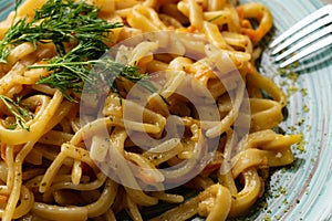 Portion of spaghetti pasta like noodles with fried vegetables on a modern plate in turquoise color, with green sauce in a jar, the