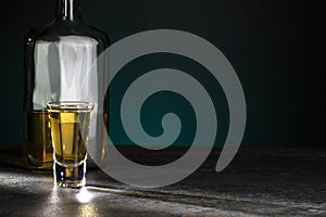 Portion of strong alcohol is brightly illuminated and half a bottle behind it on a beautiful dark background. Copy space
