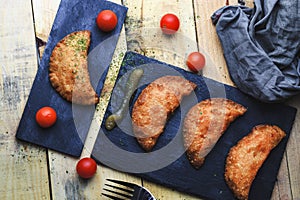 Portion and three small pasty homemade with tomatoes and applesauce on slate plate.