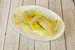 Portion of vegetable samosa served in a Hindu restaurant with iceberg lettuce and a slice of lemon with pepper