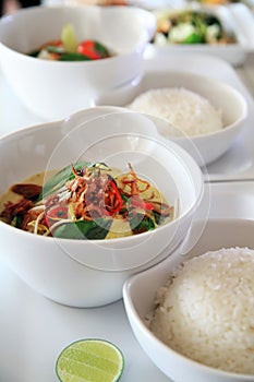 Portion vegetarian asian curry food in bowl with rice on white plate, lime as condiment