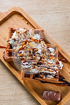 Portion of Viennese wafers with cream, chocolate, nuts, syrup and ice cream on wooden table