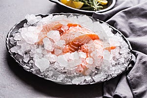 Portioned raw salmon fillets in ice on plate with lemon and rosemary