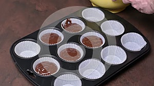 Portioning of chocolate muffin batter into paper molds in muffin tray.