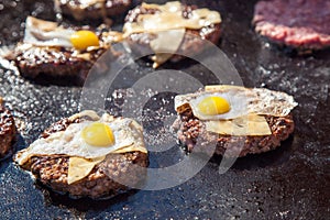 Portions of beef meat with cheese and eggs grilling on stove