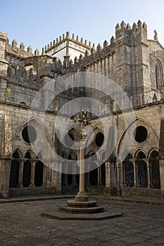 Porto cathedral seen from the inner courtyard. Old cross made of stone in the middle. Building made of stone Blue sky