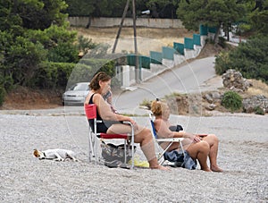 Porto Germeno, Greece. October 2020:  Two elderly women and a small dog on beautiful beach Agios Nikolaos in the Corinthian Gulf o