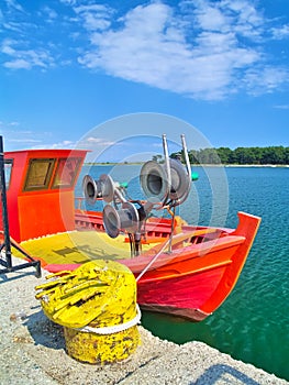 Porto Lagos, Greece, fresh painted vivid orange boat and yellow metal cordage under blue sky with clouds