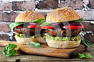 Portobello mushroom vegan burgers on a wood serving board against a dark brick background