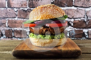 Portobello mushroom vegetarian burger on a wood serving board against a dark brick background