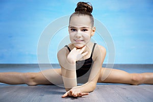 A portpait girl gymnast in a black gymnastic swimsuit is sitting on a cross splits