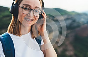 Portpait smiling young woman traveler with backpack and hipster glasses listening to favorite music on wireless headphones